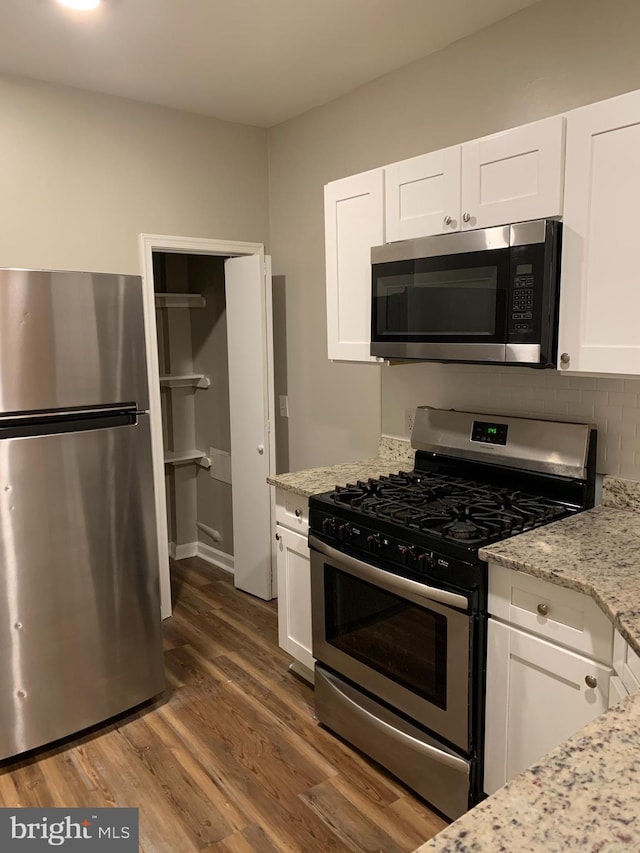 kitchen with light stone counters, white cabinets, stainless steel appliances, and dark hardwood / wood-style floors