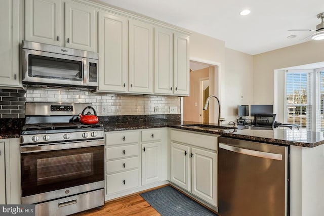 kitchen featuring kitchen peninsula, stainless steel appliances, dark stone countertops, and sink