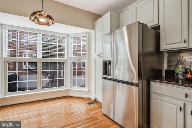 kitchen featuring white cabinetry, tasteful backsplash, stainless steel refrigerator with ice dispenser, dark stone counters, and decorative light fixtures