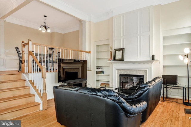 living room with built in shelves, an inviting chandelier, a high end fireplace, crown molding, and light hardwood / wood-style floors