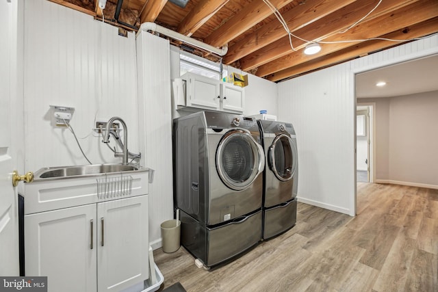 laundry area with light wood-type flooring, cabinets, washing machine and clothes dryer, and sink