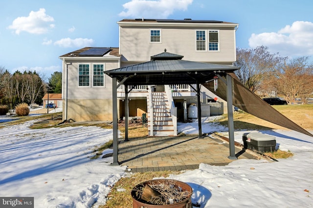 snow covered house with a gazebo, a fire pit, and solar panels