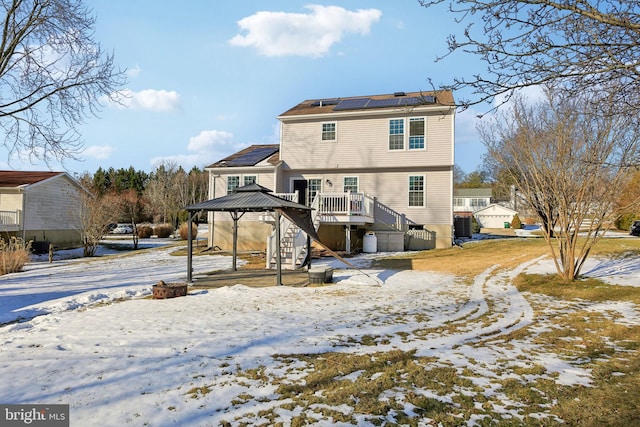 snow covered back of property featuring a wooden deck, a gazebo, and solar panels