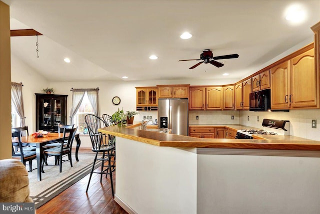 kitchen with ceiling fan, dark hardwood / wood-style flooring, kitchen peninsula, a breakfast bar, and black appliances