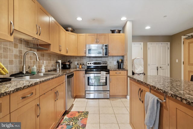 kitchen featuring appliances with stainless steel finishes, backsplash, dark stone counters, sink, and light tile patterned flooring