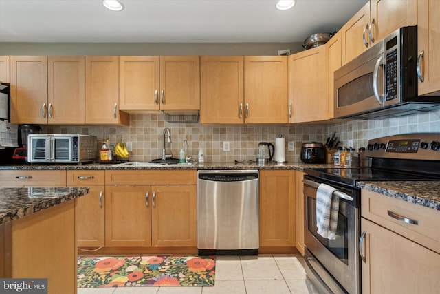 kitchen featuring decorative backsplash, appliances with stainless steel finishes, sink, dark stone countertops, and light tile patterned flooring