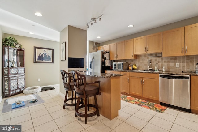 kitchen with dark stone counters, sink, light tile patterned floors, appliances with stainless steel finishes, and a kitchen island