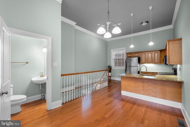 kitchen with light stone countertops, stainless steel fridge, crown molding, sink, and hanging light fixtures