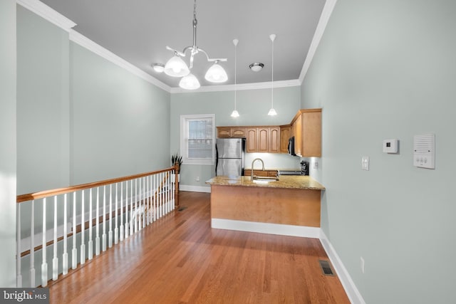 kitchen featuring stainless steel fridge, hanging light fixtures, light stone counters, and ornamental molding