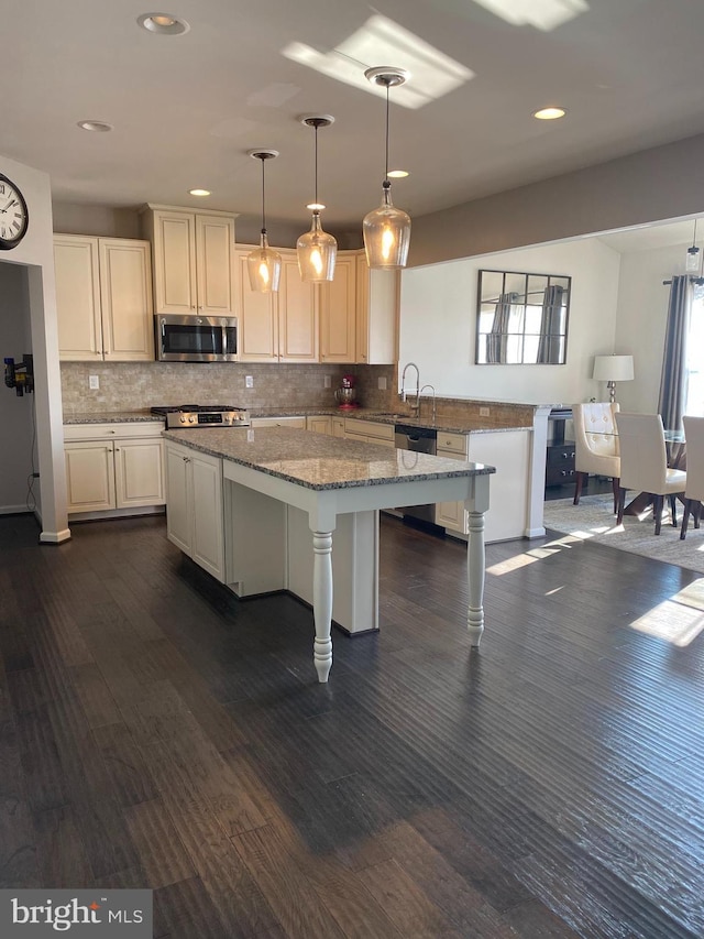 kitchen featuring a kitchen island, appliances with stainless steel finishes, a breakfast bar, decorative light fixtures, and light stone counters