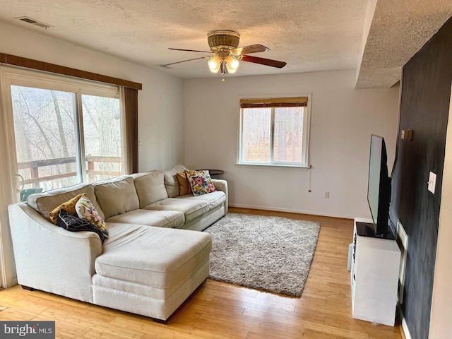 living room with ceiling fan, a wealth of natural light, a textured ceiling, and light hardwood / wood-style flooring