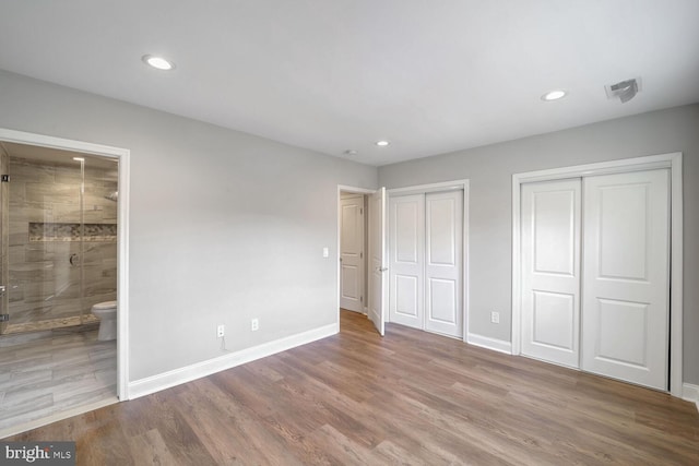 unfurnished bedroom featuring ensuite bathroom, light hardwood / wood-style floors, and two closets