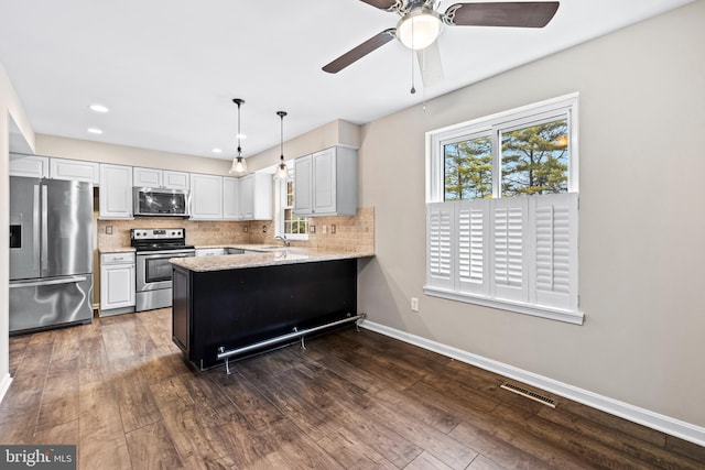 kitchen with kitchen peninsula, stainless steel appliances, sink, decorative light fixtures, and white cabinetry