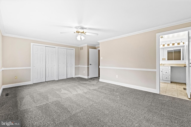 unfurnished bedroom featuring carpet, ensuite bathroom, two closets, ceiling fan, and crown molding