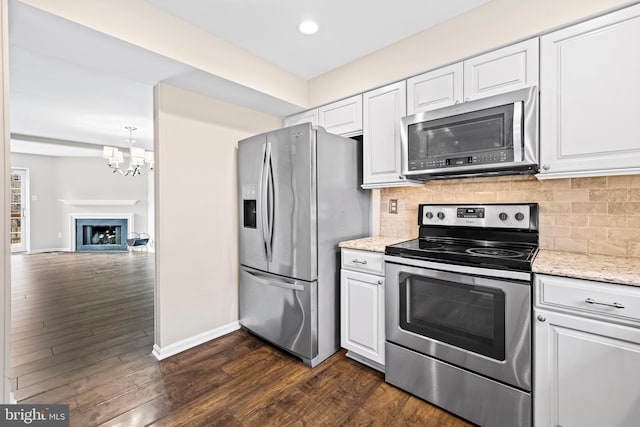 kitchen featuring light stone countertops, white cabinetry, dark wood-type flooring, stainless steel appliances, and a notable chandelier