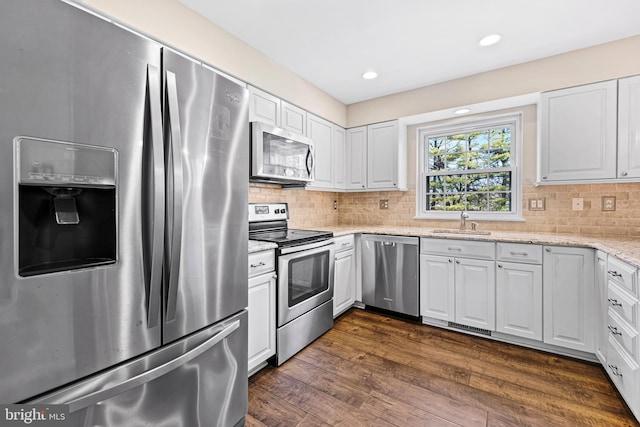 kitchen featuring sink, dark hardwood / wood-style floors, light stone countertops, appliances with stainless steel finishes, and white cabinetry