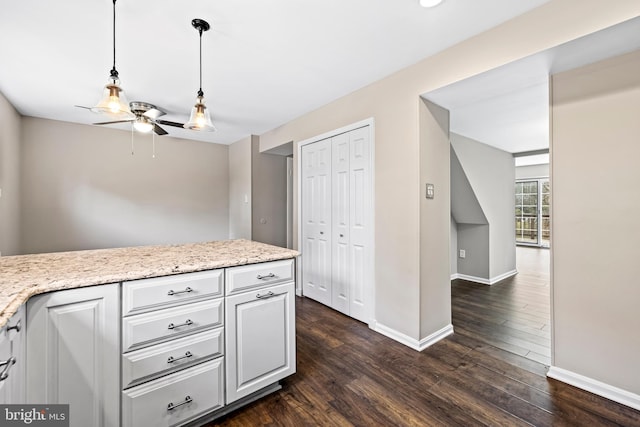 kitchen featuring white cabinetry, ceiling fan, hanging light fixtures, dark wood-type flooring, and light stone counters