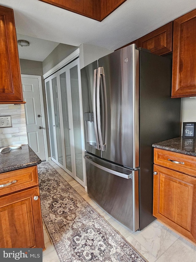 kitchen with brown cabinetry, dark stone countertops, marble finish floor, and stainless steel fridge with ice dispenser