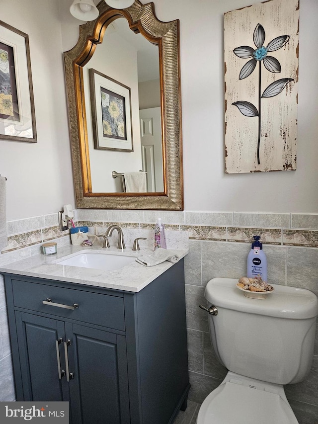 half bath with vanity, tile walls, toilet, and a wainscoted wall