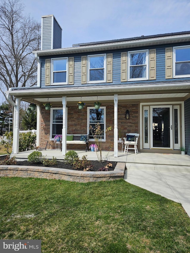 view of front facade featuring stone siding, covered porch, a chimney, and a front lawn