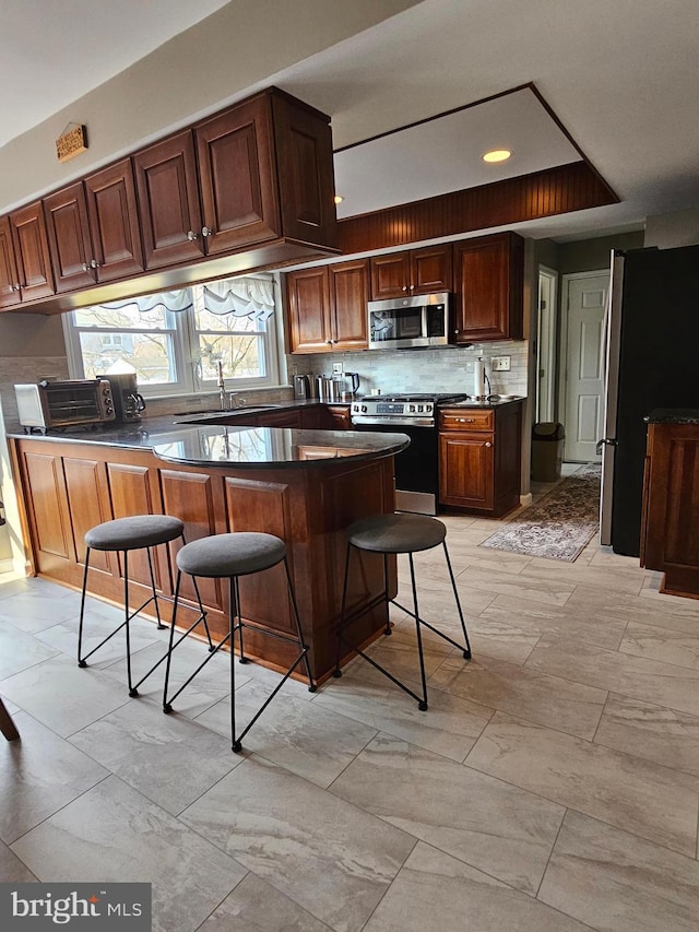 kitchen with dark countertops, backsplash, a toaster, appliances with stainless steel finishes, and a kitchen breakfast bar