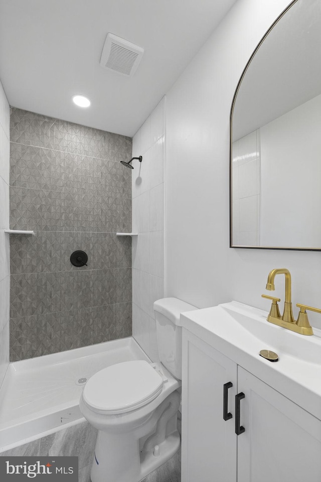 bathroom featuring a tile shower, hardwood / wood-style flooring, vanity, and toilet