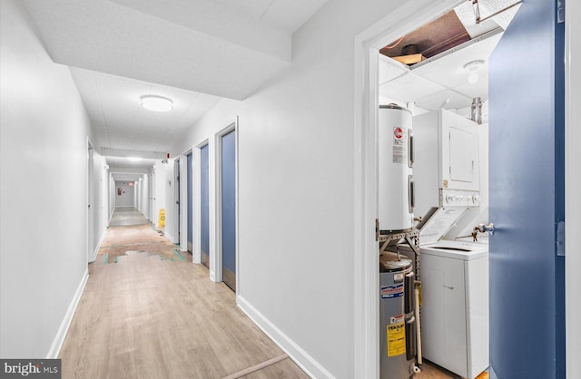 hallway featuring stacked washer / dryer, electric water heater, and light hardwood / wood-style floors