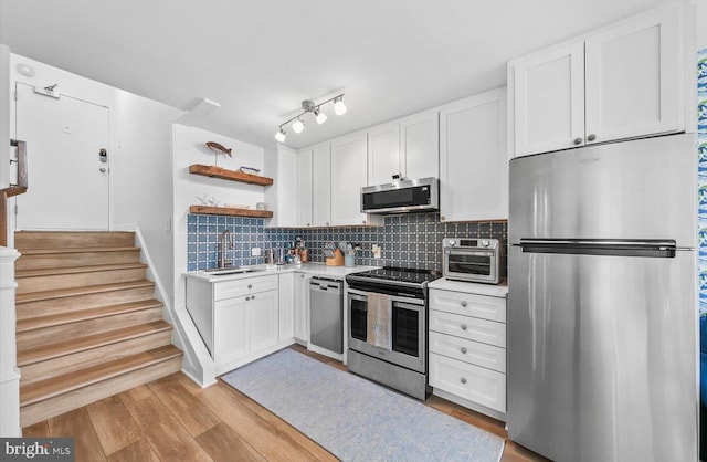 kitchen with backsplash, white cabinets, sink, appliances with stainless steel finishes, and light hardwood / wood-style floors