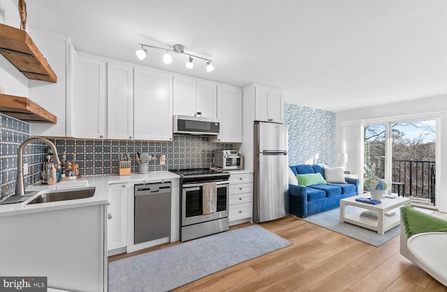 kitchen featuring backsplash, sink, light hardwood / wood-style flooring, appliances with stainless steel finishes, and white cabinetry