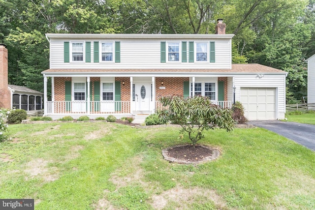 colonial house with a porch, a front yard, and a garage