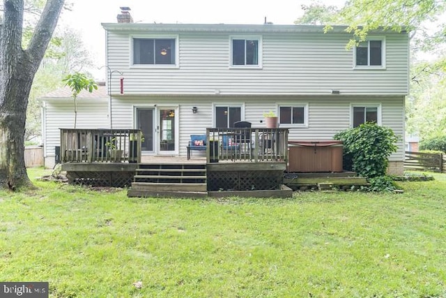 back of property with a hot tub, a deck, and a lawn