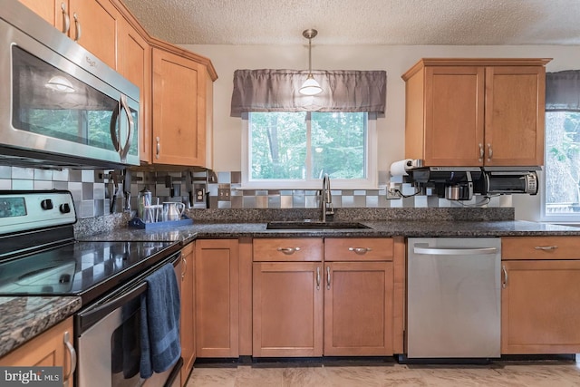 kitchen featuring stainless steel appliances, hanging light fixtures, a textured ceiling, plenty of natural light, and sink