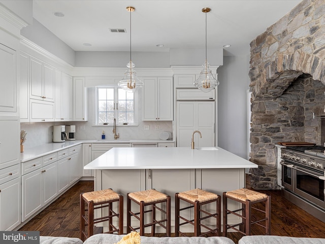 kitchen with sink, a kitchen breakfast bar, backsplash, an island with sink, and double oven range