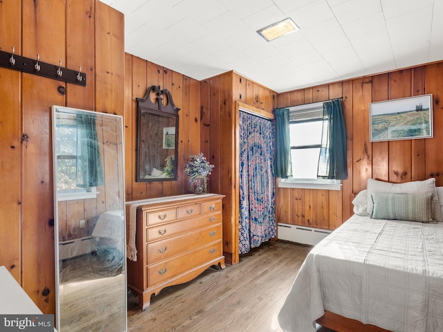 bedroom featuring baseboard heating, wood walls, and light hardwood / wood-style floors