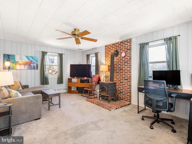 living room featuring light colored carpet, a wood stove, ceiling fan, and a baseboard heating unit