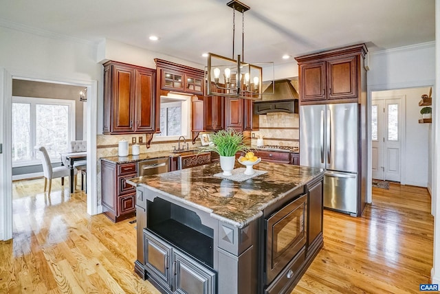 kitchen featuring a wealth of natural light, ventilation hood, backsplash, a kitchen island, and appliances with stainless steel finishes