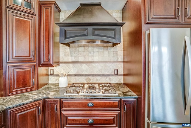 kitchen featuring appliances with stainless steel finishes, backsplash, premium range hood, and dark stone countertops