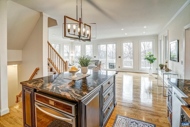 kitchen featuring ornamental molding, light hardwood / wood-style flooring, dark stone countertops, a chandelier, and a kitchen island