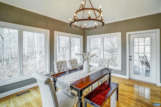 dining area featuring wood-type flooring, an inviting chandelier, a wealth of natural light, and crown molding