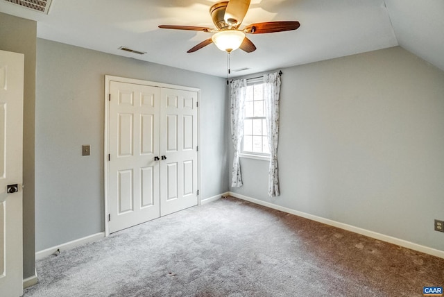 unfurnished bedroom featuring ceiling fan, light colored carpet, lofted ceiling, and a closet