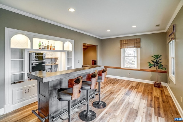 kitchen featuring light hardwood / wood-style flooring, built in features, black oven, a breakfast bar, and ornamental molding