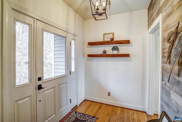 doorway to outside with light hardwood / wood-style floors, wooden walls, and a notable chandelier