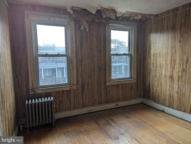 empty room featuring wood walls, radiator heating unit, and hardwood / wood-style flooring