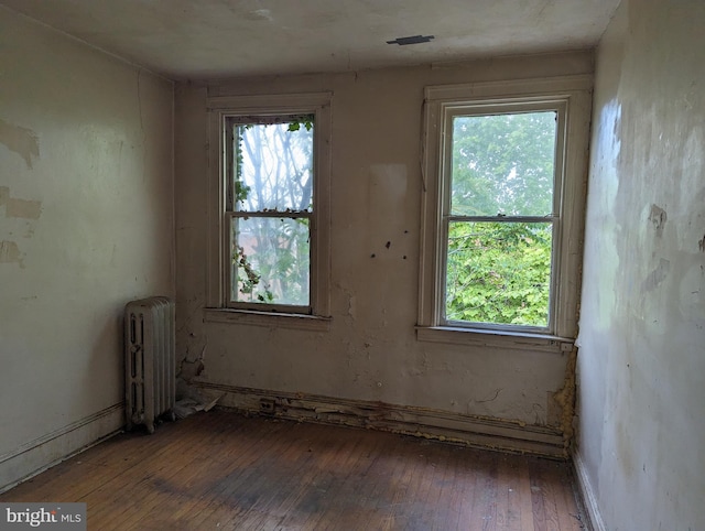 unfurnished room featuring a wealth of natural light, dark hardwood / wood-style floors, and radiator