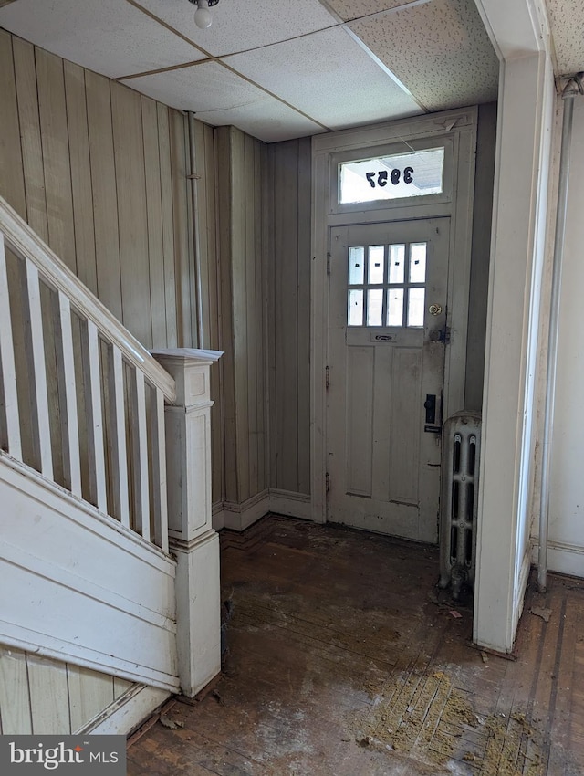 entrance foyer with wood walls, a drop ceiling, and radiator heating unit