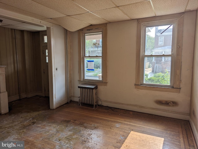 empty room featuring a wealth of natural light, a paneled ceiling, radiator, and wood-type flooring