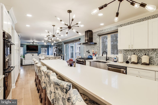 kitchen featuring appliances with stainless steel finishes, a breakfast bar, wall chimney range hood, white cabinets, and hanging light fixtures