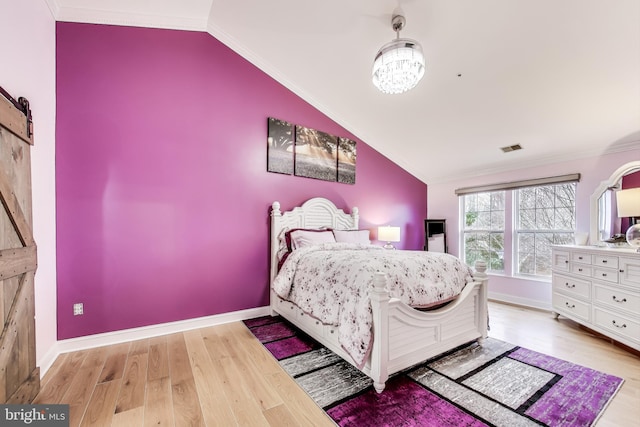 bedroom with a barn door, lofted ceiling, ornamental molding, and light hardwood / wood-style flooring