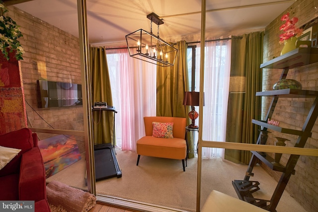 living area featuring a notable chandelier, carpet floors, and brick wall