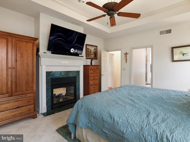 bedroom with a raised ceiling, ceiling fan, a multi sided fireplace, crown molding, and light colored carpet